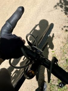 Overhead view of bicycle handlebars, a coil lock, and gloved hands on a sunny day over a crushed gravel trail. Photo by the author.